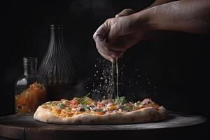 Pizza chef hand sprinkles salt on a pizza on a black background, In a close-up view, the hands of a chef skillfully assemble a delicious photo