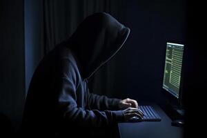 Hooded hacker using computer in dark room. Cybercrime concept, An anonymous hooded hacker full rear view coding on computer, photo