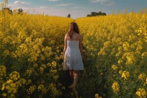 A young woman in a white dress walks through a field of yellow flowers. A young girl full rear view walks in a field of mustard flowers, photo