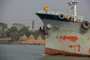 Ship with tire and rusty metal anchors going through a river. Old and rusty cargo ship front view. Old waterway vessel and tanker ship on a river. Water transportation and logistics concept on a canal photo