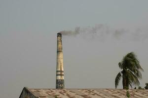 Brick kiln and industrial area scenery with blue sky. Scenic scenery of a brick kiln and a palm tree. A beautiful rural area factory and mills. Huge brick kiln creating smoke with scenic sky view. photo