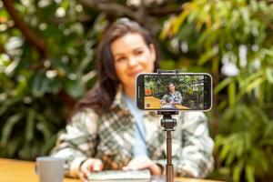 un mujer blogger registros sí misma en un teléfono inteligente cámara en pie en un trípode. persona de libre dedicación, comunicación vía el Internet. foto