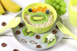 Funny bowl of oatmeal with frog faces made from fruits and berries. Food idea for kids, top view photo