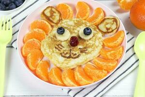 Pancakes in the shape of a funny lion with mandarin slices. A creative idea for a fun kids dessert or breakfast photo