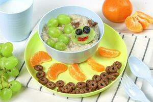 Funny bowl of oatmeal with fruits and berries caterpillar on a white wooden background. Food idea for kids, top view. photo