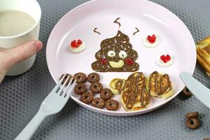 un creativo idea para un divertido niños postre. panqueques y chocolate pegar en el formar de mierda. alegre desayuno. foto