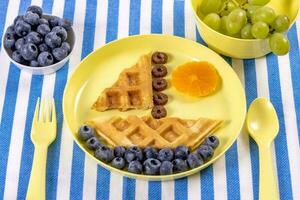 Creative idea for kids breakfast. Boat of waffles with blueberries and tangerines. photo