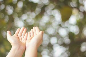 Closeup of child open two empty hands with palms up for pray to God and blessing on green blur background photo