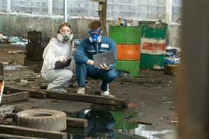 emergencia contaminación fábrica concepto. ingenieros vistiendo mecánico monos y ppe y gas mascaras inspeccionar petróleo en el fábrica piso. foto