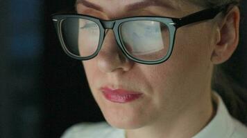 Woman in glasses looking on the monitor and and working with charts and analytics. The monitor screen is reflected in the glasses. Work at night. Home Office. Remote work video