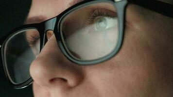 Woman in glasses looking on the monitor and and working with charts and analytics. The monitor screen is reflected in the glasses. Work at night. Home Office. Remote work video