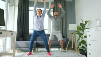 Caucasian couple is doing jumping jacks exercise at home in cozy bright room video