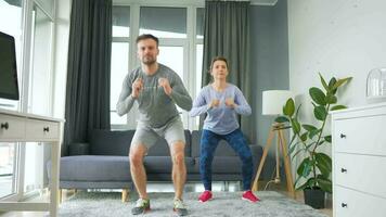 caucásico Pareja es haciendo sentadillas y patadas a hogar en acogedor brillante habitación, lento movimiento video