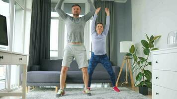 Caucasian couple is doing jumping jacks exercise at home in cozy bright room video