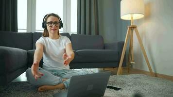 mine de rien habillé femme avec écouteurs est séance sur tapis avec portable dans confortable chambre. elle communique et travaux à distance. éloigné travail à l'extérieur le bureau. video