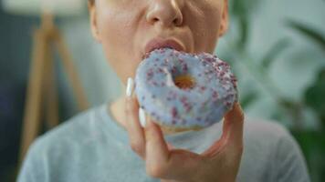 Woman eating a sweet donut in purple glaze with sprinkles. Close-up video