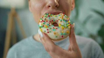 Woman eating a sweet donut in glaze with sprinkles. Close-up video