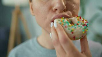 Woman eating a sweet donut in glaze with sprinkles. Close-up video