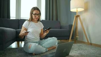 mujer con lentes es sentado en el alfombra y hace un en línea compra utilizando un crédito tarjeta y teléfono inteligente en línea compras, estilo de vida tecnología video