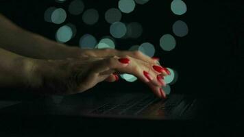 hembra manos es mecanografía en un ordenador portátil a noche. borroso luces en el antecedentes video