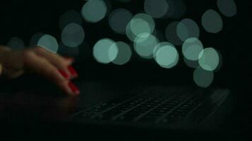 Female hands is typing on a laptop at night. Blurred lights on the background video