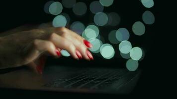 Female hands is typing on a laptop at night. Blurred lights on the background video