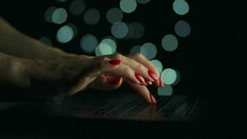 hembra manos es mecanografía en un ordenador portátil a noche. borroso luces en el antecedentes video