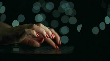 fêmea mãos é digitando em uma computador portátil às noite. borrado luzes em a fundo video