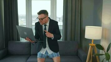 Caucasian man dressed in a jacket and underwear using laptop to make a video call from home in a modern apartment