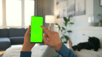 kvinna på Hem liggande på en säng och använder sig av smartphone med grön mock-up skärm i vertikal läge. video