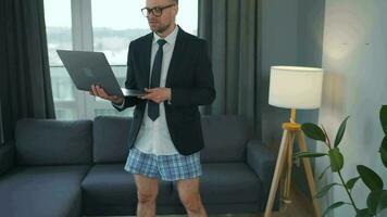 Caucasian man dressed in a jacket and underwear using laptop to make a video call from home in a modern apartment