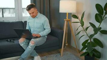 Mann mit Brille Sitzung auf das Sofa mit Laptop und Arbeiten im gemütlich Zimmer. Fernbedienung Arbeit draußen das Büro video