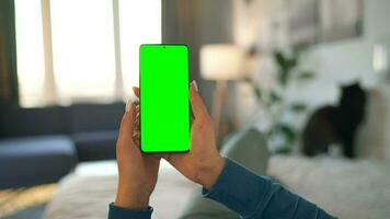 Woman at home lying on a bed and using smartphone with green mock-up screen in vertical mode. video