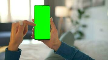 Woman at home lying on a bed and using smartphone with green mock-up screen in vertical mode. video