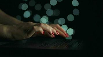Female hands is typing on a laptop at night. Blurred lights on the background video