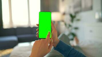 Woman at home lying on a bed and using smartphone with green mock-up screen in vertical mode. video