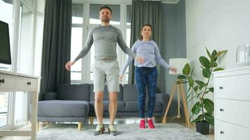 Caucasian couple is doing jumping jacks exercise at home in cozy bright room video