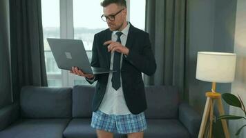 Caucasian man dressed in a jacket and underwear using laptop to make a video call from home in a modern apartment