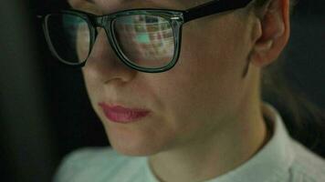 Woman in glasses looking on the monitor and and working with charts and analytics. The monitor screen is reflected in the glasses. Work at night. Home Office. Remote work video