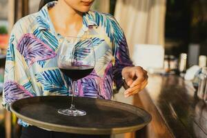 Waitress serving  glass of red wine on a tray. photo