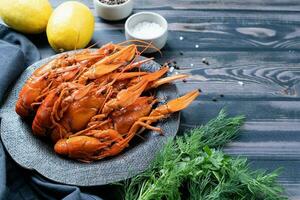 cooked crawfish on black plate with lemons and spices on wooden background photo