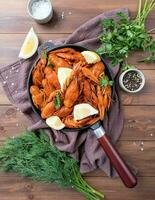 cooked crawfish in black saucepan with lemons and spices on wooden background photo