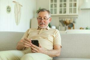 Happy middle aged senior man holding using smartphone touch screen typing scroll page. Stylish older mature beard grandfather with cell phone using internet social media apps at home. Shopping online. photo