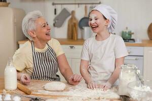 Happy family in kitchen. Grandmother and granddaughter child cook in kitchen together. Grandma teaching kid girl knead dough bake cookies. Household teamwork helping family generations concept. photo