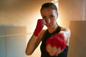 Women self defense girl power. Strong woman fighter punching with red boxing wraps sports protective bandages. Girl punching training punches looking concentrated straight. Fit body workout. photo