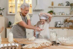 Happy family in kitchen. Grandmother and granddaughter child cook in kitchen together. Grandma teaching kid girl knead dough bake cookies. Household teamwork helping family generations concept. photo