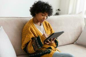 African american girl holding digital tablet touch screen typing scroll page at home. Woman with mobile tech device surfing internet using social media apps playing game. Study work shopping online. photo