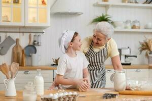 Happy family in kitchen. Grandmother and granddaughter child cook in kitchen together. Grandma teaching kid girl knead dough bake cookies. Household teamwork helping family generations concept. photo