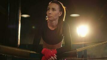 mujer combatiente niña fuerza. mujer combatiente con rojo boxeo envuelve protector vendajes en pie en boxeo anillo propensión en cuerdas esperando descansando fuerte poderoso muchacha. fuerza ajuste cuerpo rutina de ejercicio capacitación. foto