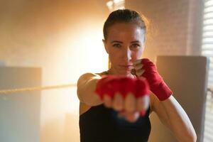 Women self defense girl power. Strong woman fighter punching with red boxing wraps sports protective bandages. Girl punching training punches looking concentrated straight. Fit body workout. photo